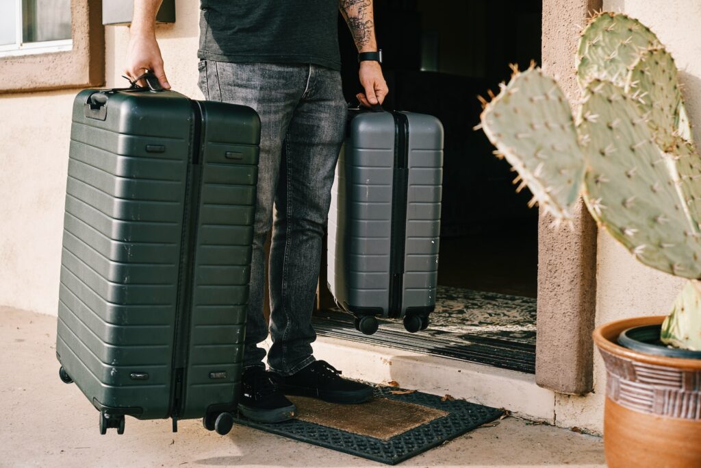 man in black denim jeans and black leather shoes standing beside black luggage bag